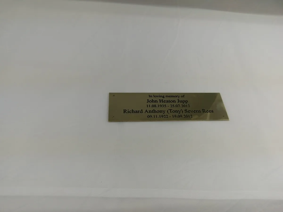 Engraved brass memorial plaque with two names and dates, photographed before fitting