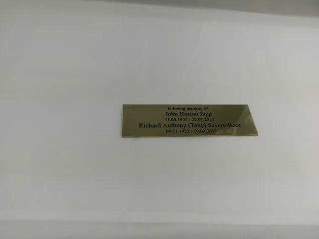 Engraved brass memorial plaque with two names and dates, photographed before fitting