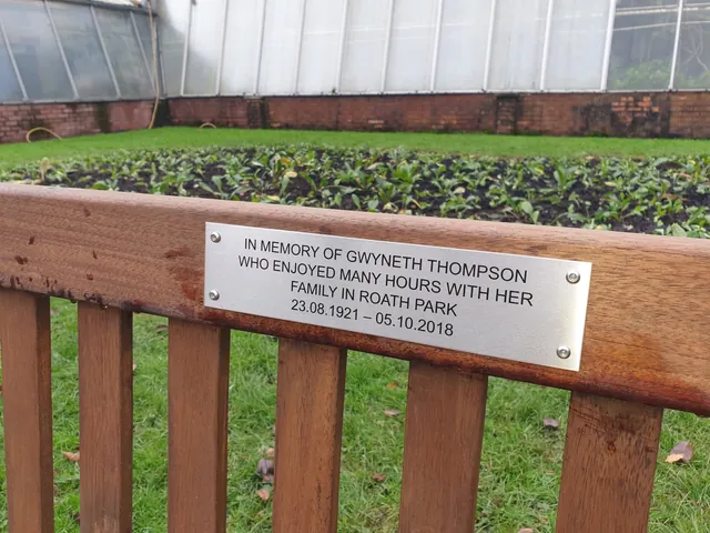 Stainless steel memorial plaque on a wooden bench in Roath Park, Cardiff